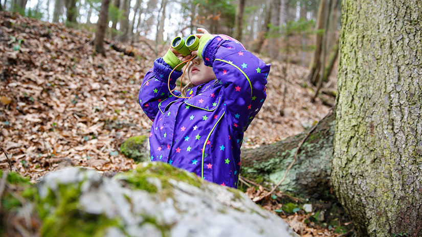 Student in the woods holding binoculars
