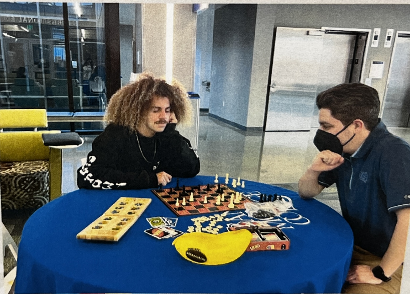 two people staring at a chess board and other board games on the table